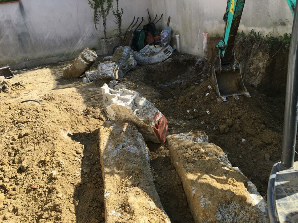 Chantier de démolition avec mini-pelle, gravats et anciennes fondations dégagées