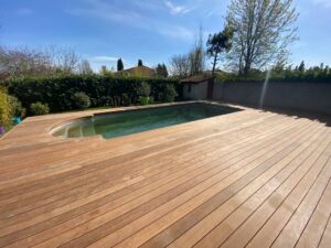 Terrasse en bois entourant une piscine dans un jardin ensoleillé d'Occitanie