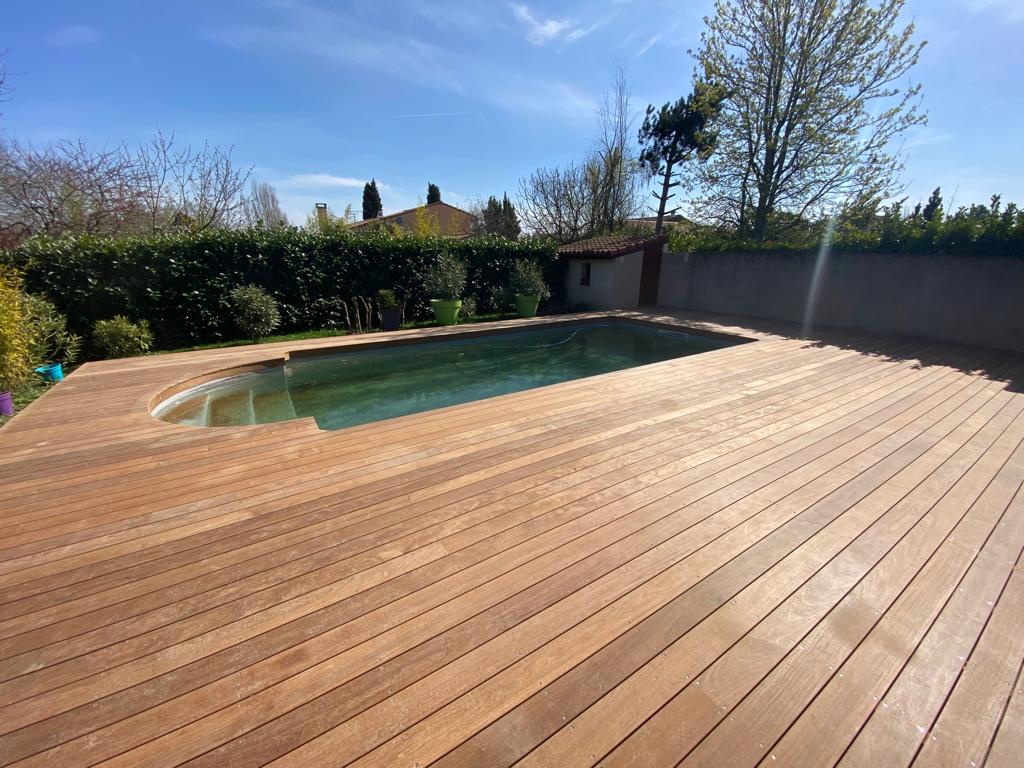 Terrasse en bois entourant une piscine dans un jardin ensoleillé d'Occitanie